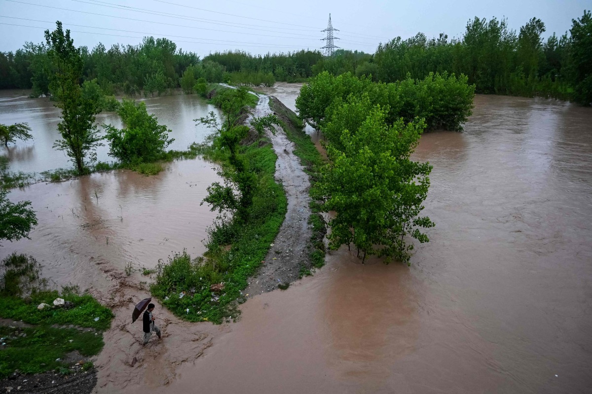 A man walks along a flooded path as torrential rains cause water channels to overflow, inundating nearby areas of Peshawar on April 7, 2026. Photo by Abdul MAJEED / AFP