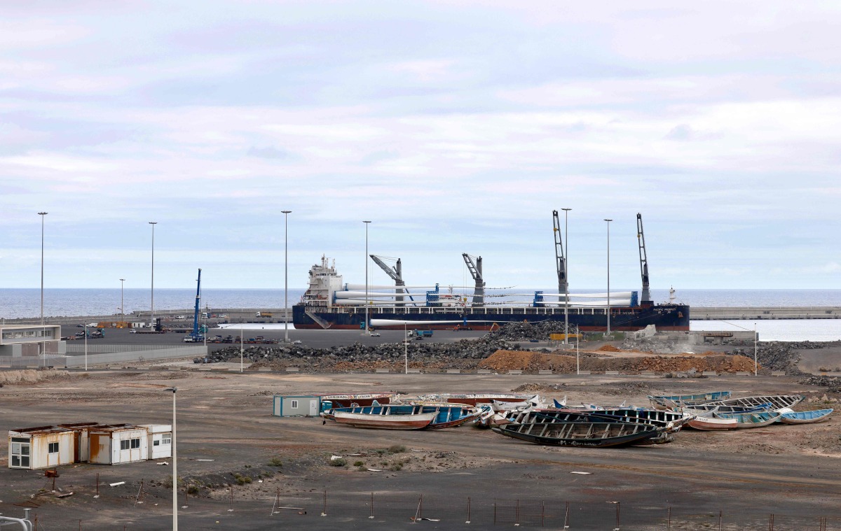 A large cargo ship is seen behind migrant boats stacked at the port of Granadilla de Abona, on the island of Tenerife in Spain's Canary Islands archipielago, on May 6, 2026. (Photo by Oscar DEL POZO / AFP)
