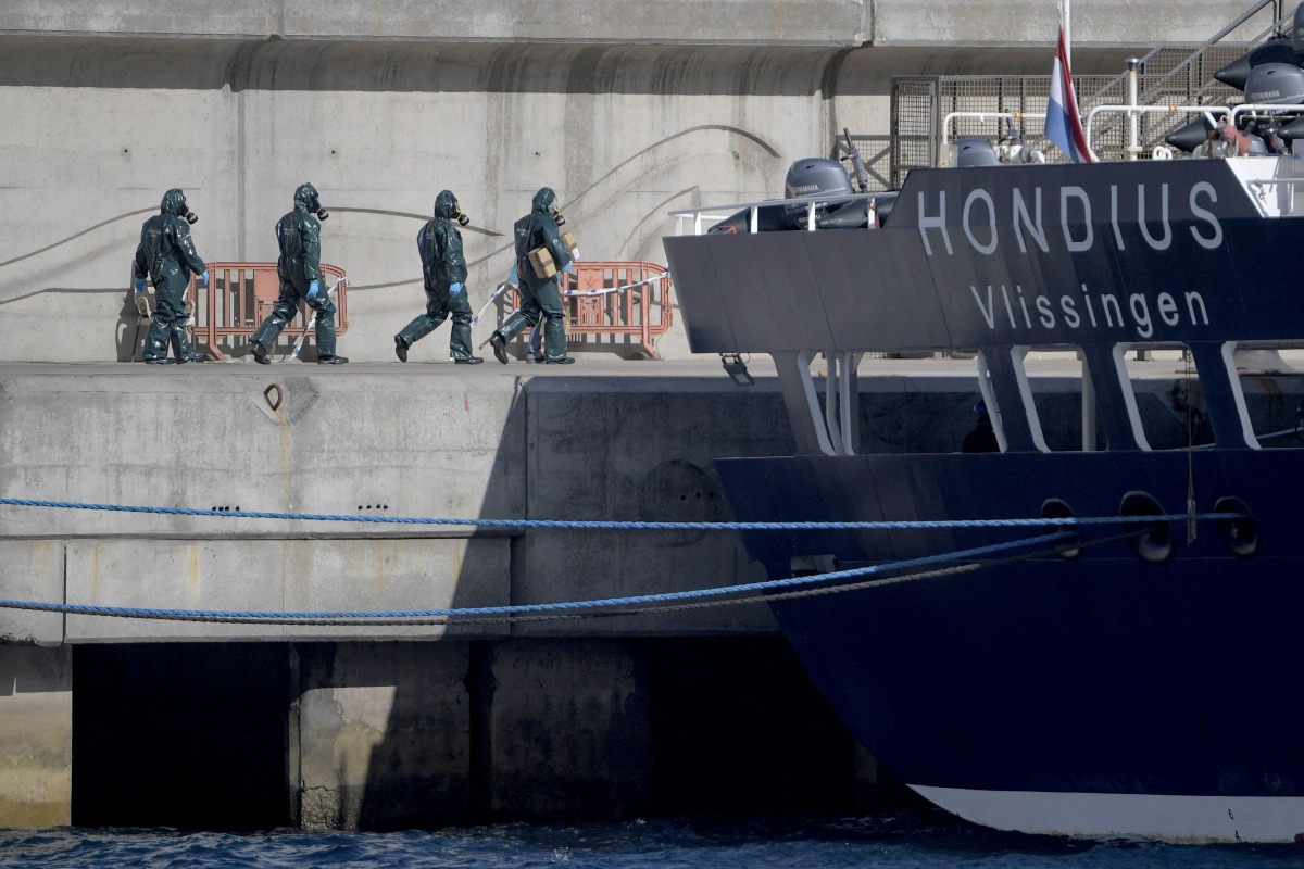 Persons wearing protective suits walk toward the hantavirus-stricken cruise ship MV Hondius docked in the port of Granadilla de Abona on the island of Tenerife in Spain's Canary Islands on May 11, 2026. (Photo by JORGE GUERRERO / AFP)