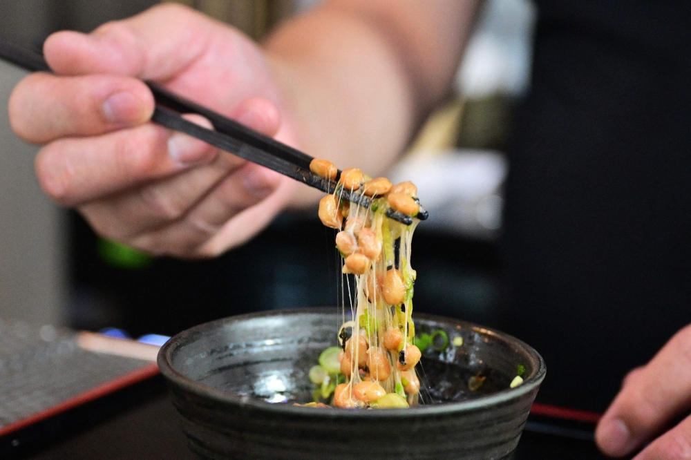 Kenji Suzuki, second-generation owner of Suehiro Japanese Restaurant in Los Angeles, California, lifting natto from a bowl with chopsticks. (Photo by Frederic J. Brown / AFP) 