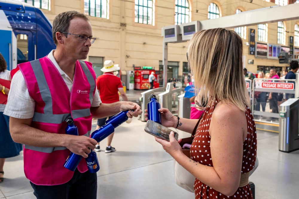 A staff member hands out flasks to customers as part of a distribution of water bottles, hats and fans at the Saint-Charles railway station in Marseille on June 22, 2026. (Photo by Miguel Medina / AFP)