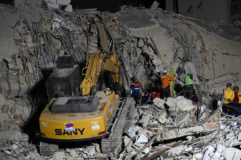 Rescue teams operate heavy machinery at the site of a collapsed building in Caracas on June 25, 2026, following earthquakes. (Photo by Juan Barreto/ AFP)