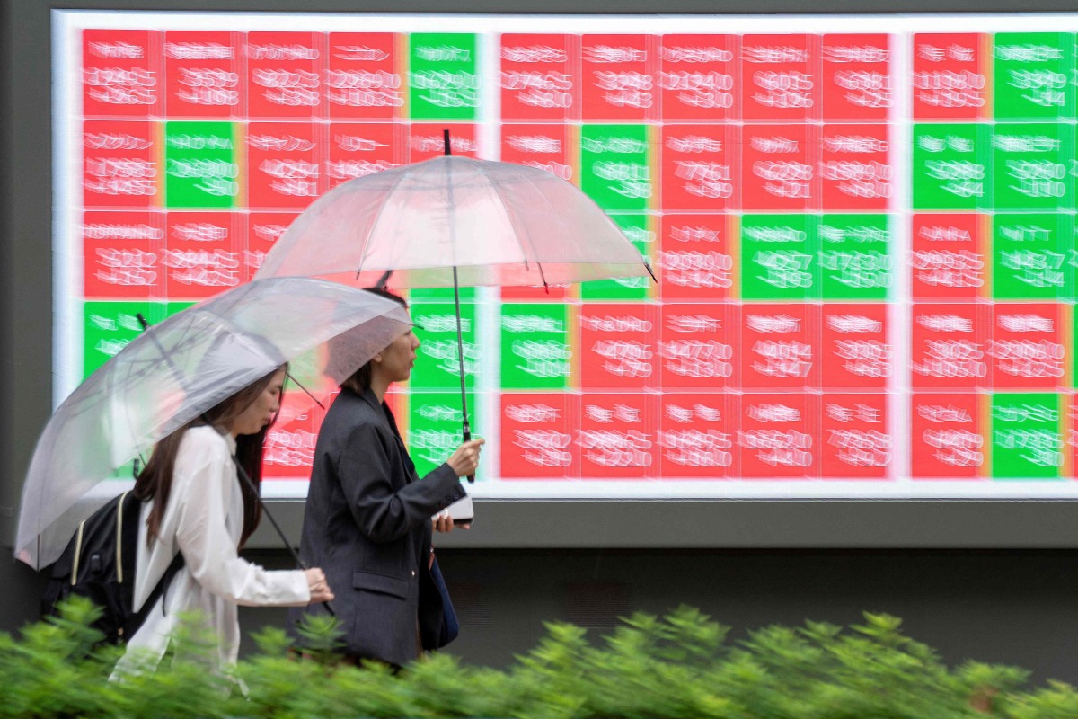 Pedestrians walk past an electronic quotation board displaying the Nikkei 225 stock prices on the Tokyo Stock Exchange along a street in Tokyo on June 25, 2026. (Photo by Kazuhiro NOGI / AFP)