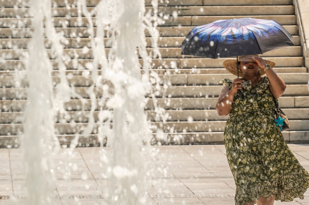 A woman protects herself from the sun with an umbrella as she walks through Athens' main square of Syntagman on July 21, 2026. (Photo by Aris Messinis / AFP)
 