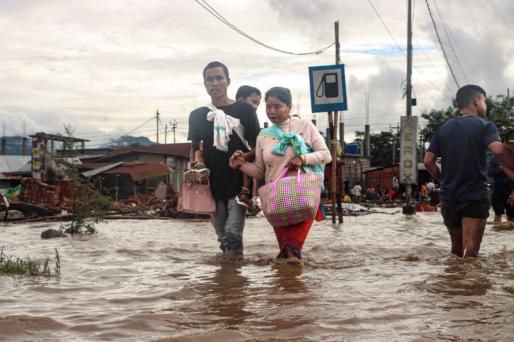 Residents wade through a flooded street near an overflowing river after heavy rains at Nambol in Bishnupur district, in India's northeastern state of Manipur on July 22, 2026. (Photo by Vishma Ahanthem / AFP)