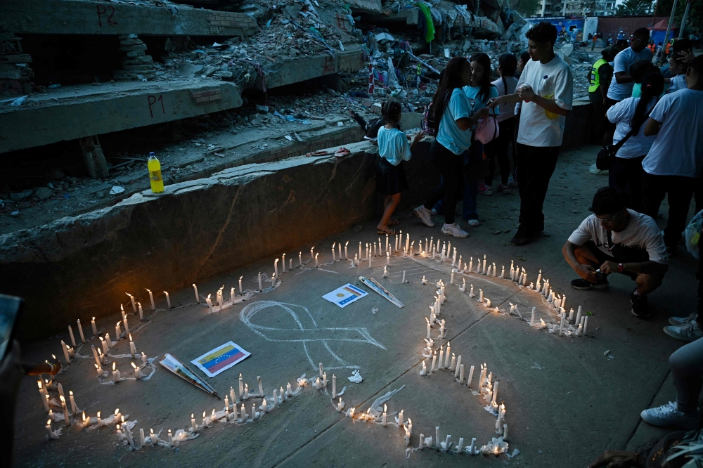 Relatives light candles during a mass for the victims in Caraballeda, Venezuela, on July 24, 2026, one month after an earthquake struck the area. (Photo by Federico PARRA / AFP)