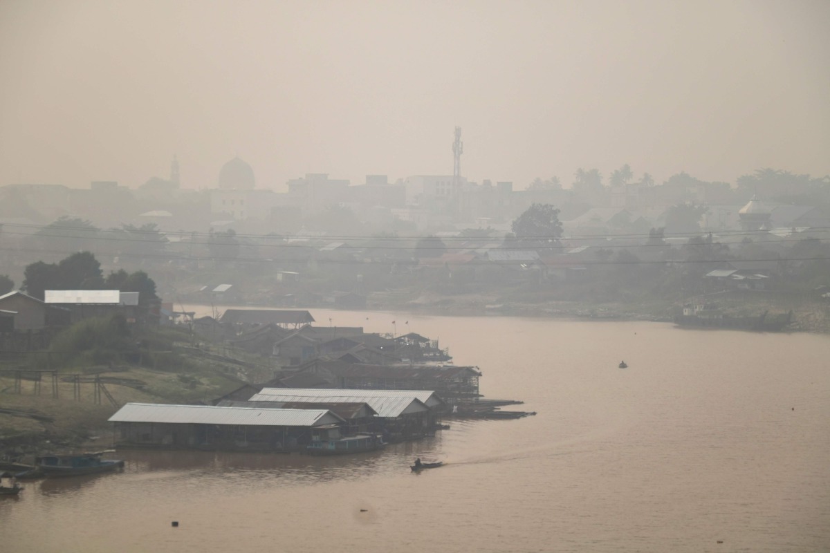 Haze blankets a riverside residential area along the Kahayan River in Palangkaraya, Central Kalimantan, on August 21, 2026, as a result of widespread forest and land fires occurring at various points across the island. (Photo by REINA / AFP)