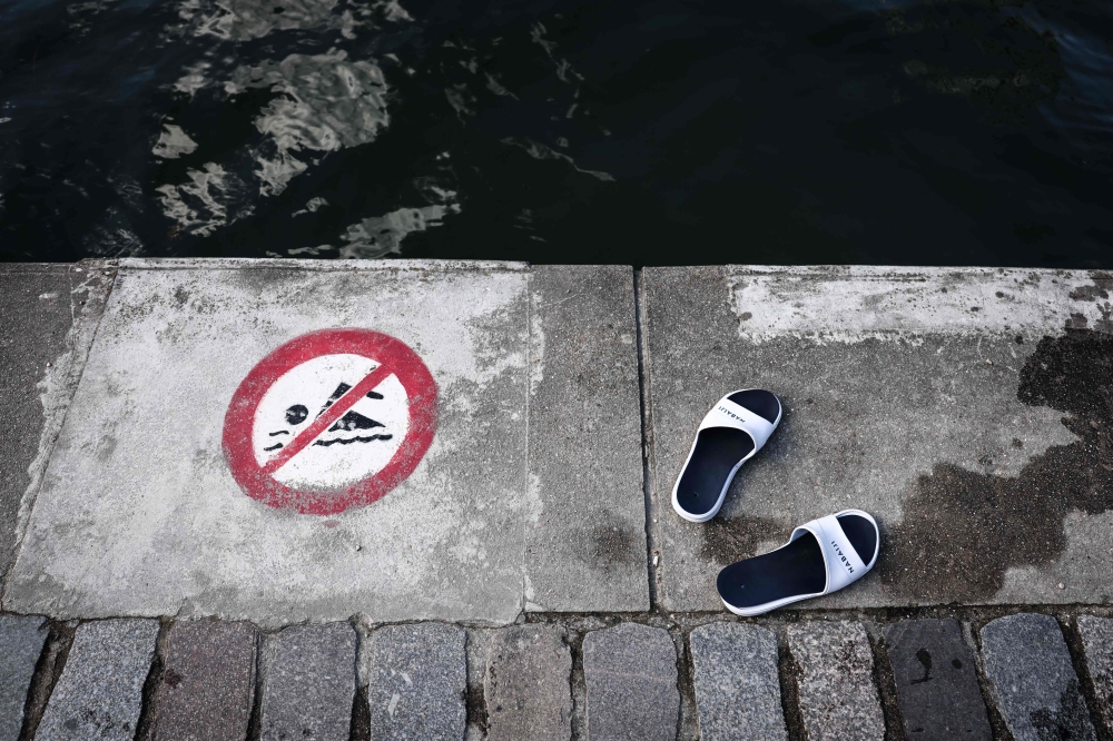 (FILES) This photograph shows sandals next to a sign indicating that swimming is forbidden, at the Bassin de la Villette during a cold water swimming event in Paris on March 29, 2025.(Photo by Thibaud MORITZ / AFP)
