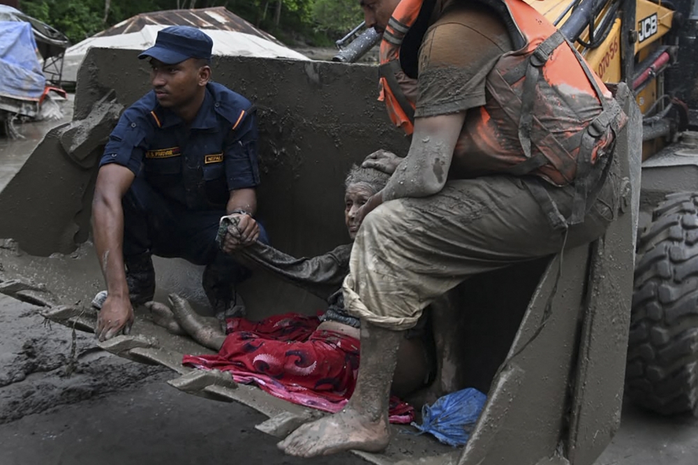 Rescue personnel use an excavator to carry a person affected by flash floods at Devghat in Nepal's Nuwakot district on August 26, 2026. (Photo by Prakash MATHEMA / AFP)
