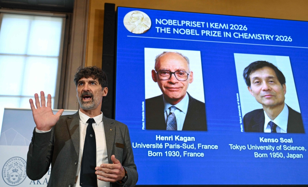 The chair of the Nobel Committee for Chemistry Heiner Linke (L) explains the field of research of Nobel Prize winners France's Henri Kagan and Japan's Kenso Soai (displayed on the screen in background) during a press conference in Stockholm, Sweden, on October 7, 2026. (Photo by Jonathan Nackstrand / AFP)