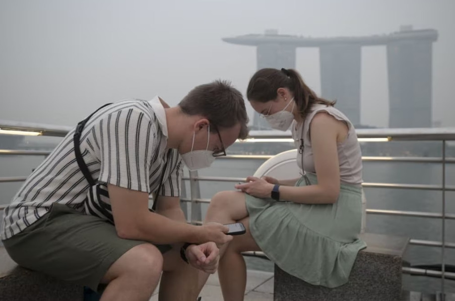 Tourists wear protective masks while seated across Marina Bay Sands in Singapore on October 15, 2026, as the country continues to be shrouded in haze caused by fires in Indonesia / AFP