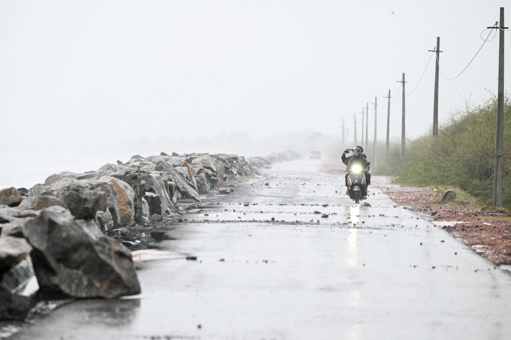 A scooterist rides along the Bay of Bengal coast during rainfall in Andhra Pradesh's Kakinada on October 27, 2026, ahead of cyclone Arnab's expected landfall. (Photo by Noah Seelam / AFP)