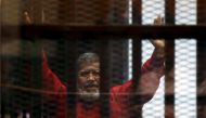 Egypt's deposed president Mohamed Mursi greets his lawyers and people from behind bars at a court wearing the red uniform of a prisoner sentenced to death, during his court appearance with Muslim Brotherhood members on the outskirts of Cairo, Egypt, on Ju