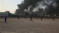 Children play football as smoke rises from oil wells, were set on fire by Islamic State to limit coalition forces pilots' eyesight and to make the wells out of service following Iraqi army's retaking of Al Qayyarah town from Islamic State during the opera