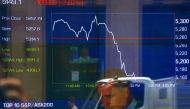 A pedestrian and financial journalist look at their phones as they are reflected in a window in front of a board displaying stock prices at the Australian Securities Exchange (ASX) in Sydney, Australia, November 9, 2016. REUTERS/David Gray