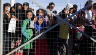 Iraqi refugees wait behind a fenced gate for food distribution at the Khazir refugee camp near the Kurdish checkpoint of Aski Kalak, 40 km West of Arbil, the capital of the autonomous Kurdish region of northern Iraq, on November 21, 2016. / AFP