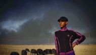 File picture of a young shepherd watching over his flock of sheep, their fleece blackened by smoke from burning oil wells set ablaze by Islamic State (IS) jihadists before retreating, near Mosul. 
