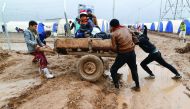 Displaced Iraqis who fled the Islamic State stronghold of Mosul, push a cart through mud following heavy rain at Khazer camp, yesterday.