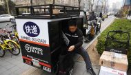 (FILES) This file photo taken on March 17, 2017 shows an SF Express courier delivery rider sorting packages in the back of his tricycle on a sidewalk in Beijing. AFP / Greg Baker
