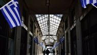 Men walk in a passage adorned with Greek flags in central Athens on March 21, 2017. / AFP / LOUISA GOULIAMAKI.