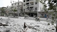 A Syrian man walks with a bicycle along a road that was destroyed in an air strike in the rebel-controlled town of Hamouria, in the eastern Ghouta region on the outskirts of the capital Damascus on May 1, 2017. / AFP / ABDULMONAM EASSA
