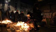 Riot police stand in front of a youngster gesturing near papers set on fire in Menilmontant district of Paris during the night on May 7, 2017 after the announcement of the French presidential election results. / AFP / Lara Priolet.