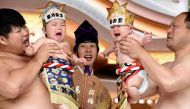 Sumo wresters hold up crying babies in front of a referee (C) clad in a traditional costume during a 