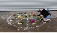 A woman places a candle at a makeshift memorial of flowers and candles arranged like a peace sign on July 29, 2017 in Hamburg, northern Germany, at the site where a man killed one person and wounded several others in a knife attack the day before. (AFP / 