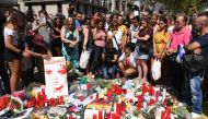 People stand next to flowers, candles and other items set up on the Las Ramblas boulevard in Barcelona as they pay tribute to the victims of the Barcelona attack, a day after a van ploughed into the crowd, killing 13 persons and injuring over 100 on Augus