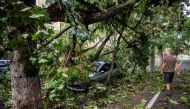 A man walks near a car that was hit by a falling tree following a storm that tore through western Romania, in Timisoara, Romania September 17, 2017. / Reuters.