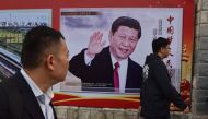People walk past a poster featuring Chinese President Xi Jinping with a slogan reading 
