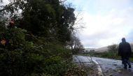 A man walks past a worker clearing fallen trees off a road during Storm Ophelia in the County Clare area of the Burren, Ireland October 16, 2017. REUTERS/Clodagh Kilcoyne
