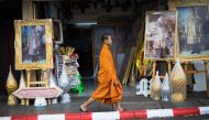 In this photograph taken on October 19, 2017, a Buddhist monk walks past framed images of Thailand's late king Bhumibol Adulyadej in front of a shop in Bangkok. The kingdom has been preparing for the cremation of the former king following his death at the