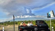 Balinese people ride on an open car past Mount Agung erupting seen from Kubu sub-district in Karangasem Regency, on Indonesia's resort island of Bali on November 27, 2017.  AFP / SONNY TUMBELAKA
