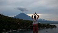 A tourist from Russia poses while a friend takes her photograph with Mount Agung volcano erupting in the background from Amed, Karangasem Regency, Bali, Indonesia, November 30, 2017. REUTERS/Darren Whiteside
