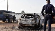 A gendarme stands in front of the wreckage of a burnt car, on January 10, 2018 in front of the CCDO elite military unit centre, a day after gunshots and heavy weapons fire erupted between rival factions within Ivory Coast army.  AFP