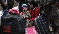 Syrian children evacuated from Eastern Ghouta sit on luggage after arriving in Qalaat al-Madiq, some 45 kilometres northwest of the central city of Hama, on March 30, 2018, following the ongoing evacuation deals made between rebel fighters and Russia, an 