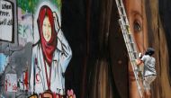 A foreign artist paints on the Israeli wall a mural depicting Palestinian teen Ahed Tamimi who is detained by Israel, next to a mural of dead Palestinian nurse Razan Al-Najar, in Bethlehem, in the occupied West Bank, July 25, 2018. Reuters/Mussa Qawasma
