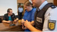 A German court handed down lengthy jail sentences to Berrin Taha (held by policeman) and her husband Christian Lais (sitting left) for pimping their son online. (Faces blurred for legal reasons to protect identify of child). AFP / THOMAS KIENZLE