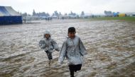 Children refugees run under the rain to get a place on the food line at their makeshift camp in the northern border village of Idomeni, Greece, on April 9, 2016. AFP/Bulent Kilic