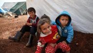 A Syrian girl holds another child as they sit with two others outsid ea tent at a camp for the displaced near the town of Sarmada in the northern countryside of the rebel-held Idlib province on December 1, 2018. AFP / Aaref Watad
 