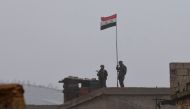 A picture taken on December 30, 2018, shows a Syrian national flag flying over a building as regime forces gather in the southern countryside of the northern Kurdish-controlled city of Manbij. AFP 