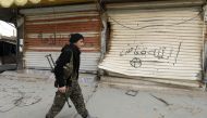 A fighter from the Syrian Democratic Forces (SDF) walks past shops with their fronts painted with the Arabic phrases 