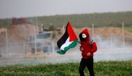 A Palestinian protester wearing a Guy Fawkes mask carries the national flag during clashes with Israeli forces following a demonstration near the fence along the border with Israel, east of Gaza City, on February 15, 2019. AFP / Said Khatib 