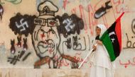 A Libyan woman holding a Kingdom of Libya flag walks past a caricature of Muammar Gaddafi near the court house in Benghazi June 8, 2011. Reuters/Esam Al-Fetori