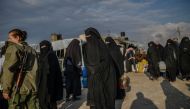 Veiled women, reportedly wives and members of the Islamic State, walk under the supervision of a female fighter from the Syrian Democratic Forces (SDF) at al-Hol camp at al-Hasakeh governorate at northeastern Syria on February 17, 2019. / AFP / BULENT KIL
