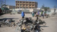 People walk near the wreckage of a car near the complex housing Somalia's ministries of works and labour stormed by Al-Shabaab militants in Somalia's capital Mogadishu on March 23, 2019.  AFP / Mohamed ABDIWAHAB
