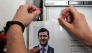 A member of a local electoral commission hangs an information placard bearing a portait of Ukrainian comedian and presidential candidate Volodymyr Zelensky as he prepares a polling station for the upcoming presidential election in Kiev, on April 20, 2019 