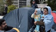 A migrant mother stands by a tent as a group of migrants and refugees camped out at the central Athens Syntagma square, on April 19, 2019, following their eviction from squatted building in Exarchia neibourhood. AFP / Louisa Gouliamaki 