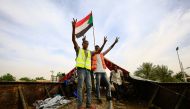 Sudanese protesters wearing yellow and orange gilets and waving a national flag stand on a closed railway track leading to the protest site in central Khartoum on May 12, 2019.   AFP / ASHRAF SHAZLY